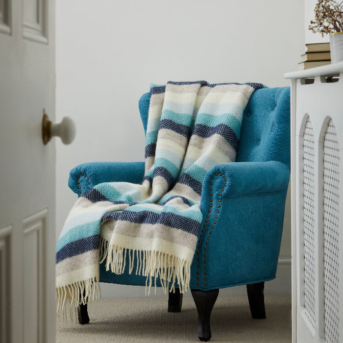 Blue armchair with a colourful striped blanket in different shades of blue, in a room with white walls and a door.