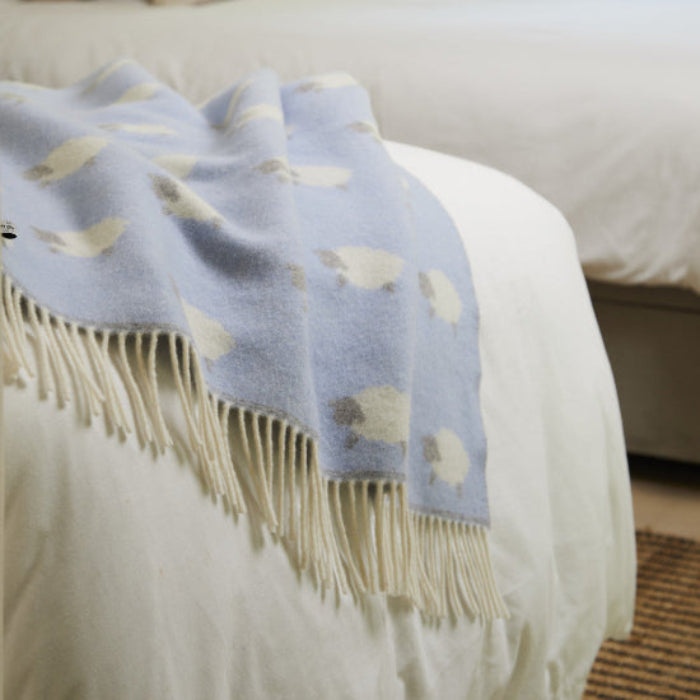 Sheep Blue Merino Wool Baby Blanket with cute sheep pattern draped over a bed in a bedroom setting.