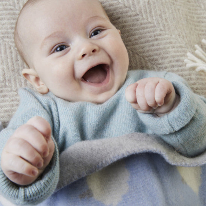 Happy baby lying on a textured surface wrapped in a Sheep Blue Merino Wool Baby Blanket