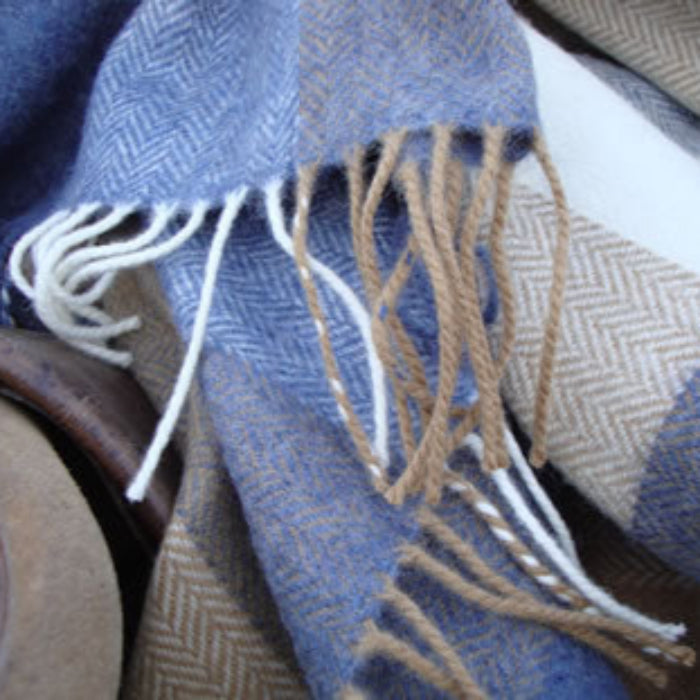 Close up of a blue, tan and beige plaid fabric throw with fringes