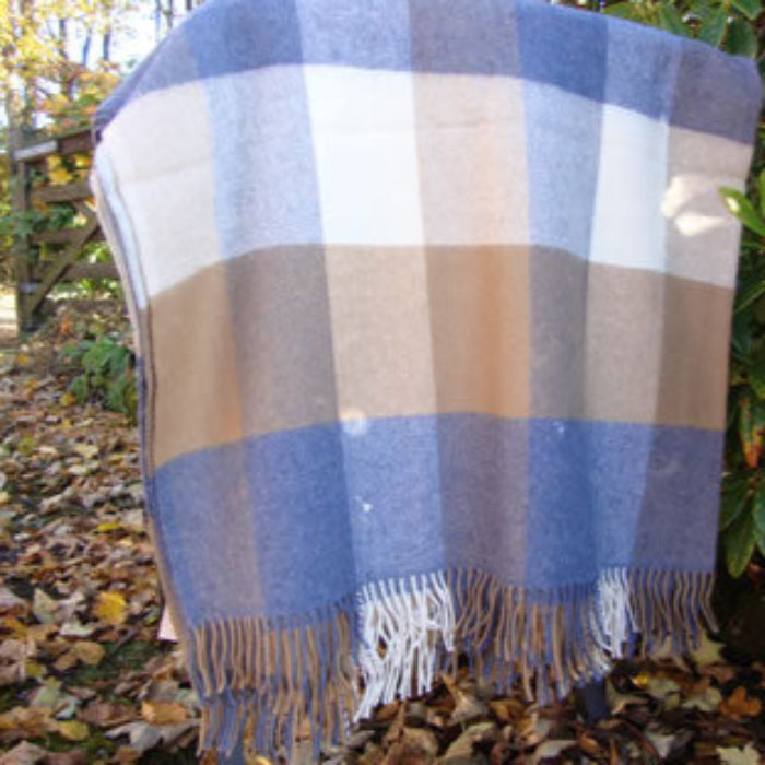 Plaid lambswool throw with blue, tan, and beige pattern in a woodland setting