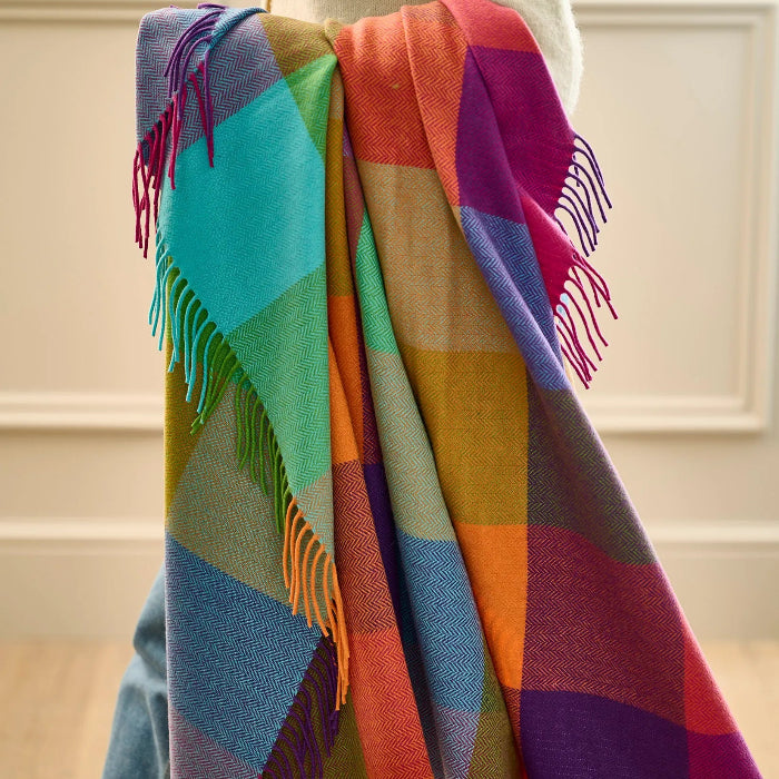 Colorful checkered cashmere mix throw with fringes being carried by a person, against a neutral background.