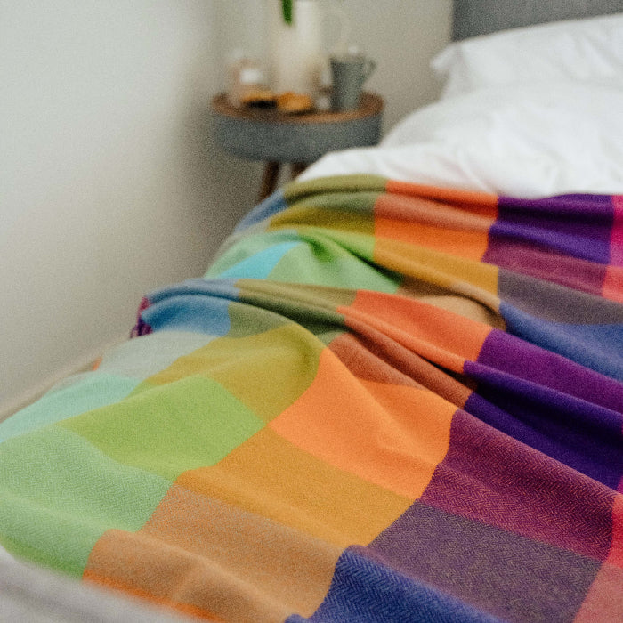Colorful checkered cashmere mix throw on a white bed with a side table in the background