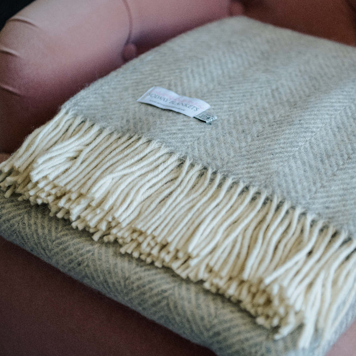 Silver grey herringbone wool blanket with fringes folded neatly on a pink chair