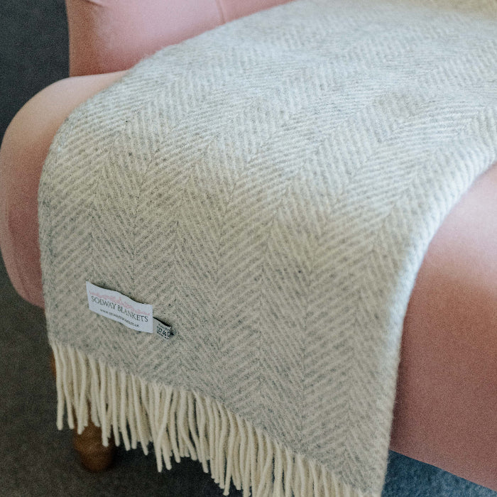 Silver grey herringbone wool blanket with fringes draped over a pink chair.