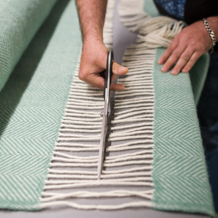 Person cutting white fringes between two green herringbone styled woolen blankets
