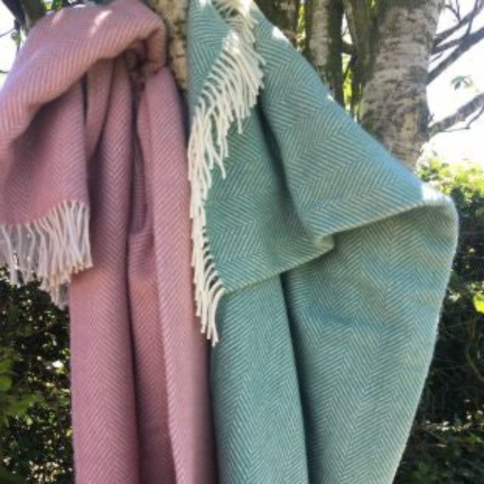 Two herringbone styled blankets, one pink and one green, draped over a tree branch with a natural background.