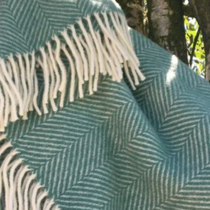 Green and white herringbone patterned blanket with fringes on a natural background