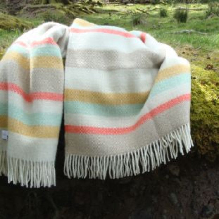 Colouful striped wool blanket with fringes draped over a rock in a natural setting