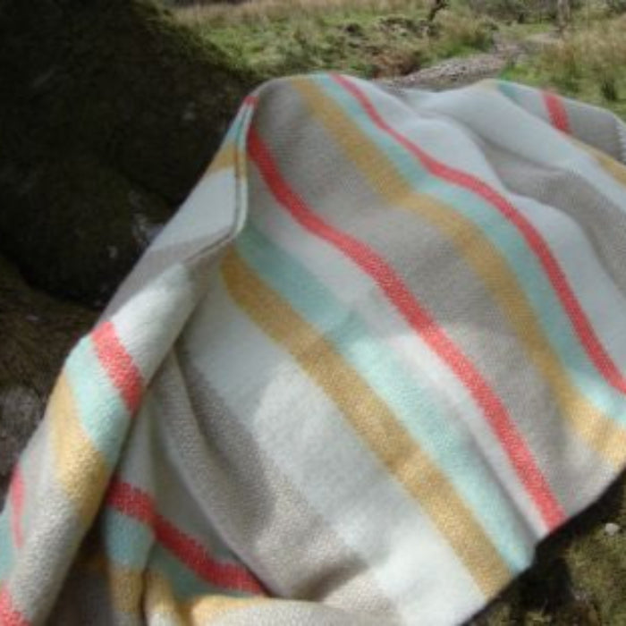 Striped wool blanket with pastel colours draped over a tree stump, in a natural background