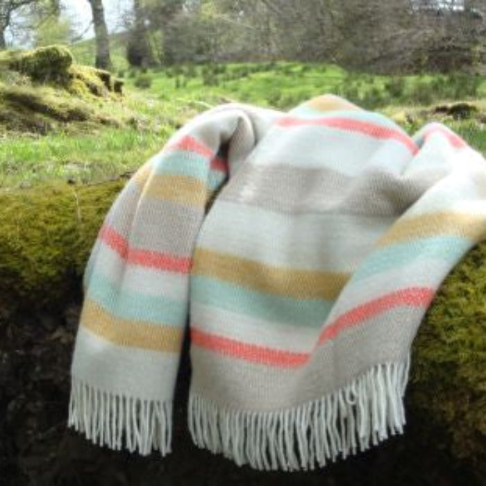Colourful striped wool blanket with fringes draped over a moss-covered rock in a natural setting