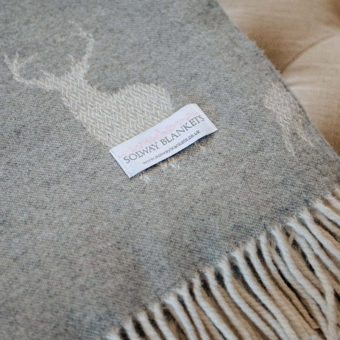 Close up of a folded grey blanket throw with embroidered stag and neutral fringes featuring a Solway Blankets label