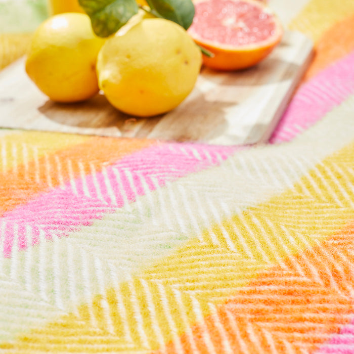 Colourful woven wool blanket with a pattern of interwoven lines in various colors - green, yellow, orange and pink, placed on a surface with lemons and a pink grapefruit.