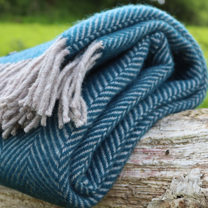Teal blue woven wool blanket with fringe, folded on a wooden log outdoors