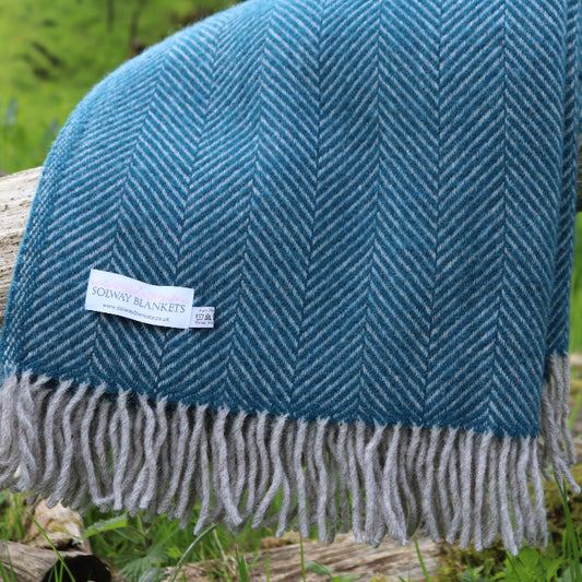Teal blue herringbone blanket with fringes featuring a 'Solway Blankets' label, draped over a log in a natural setting