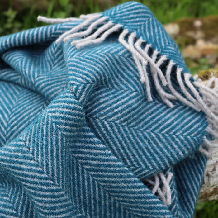 Teal blue striped wool blanket with fringes on a wooden log in a forestry setting
