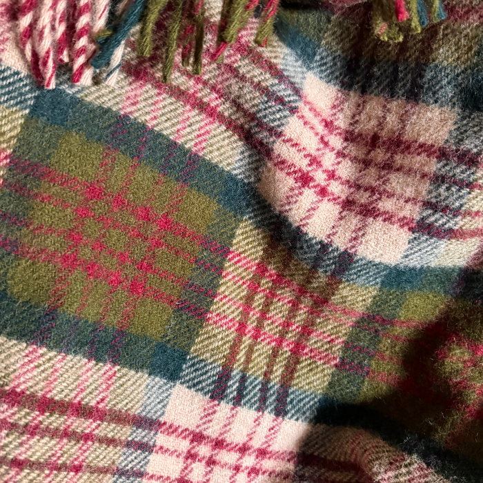 A close-up of a folded Thistleberry tartan plaid blanket. Showing the texture and colours of beige, red, moss green and bottle green in a traditional check design