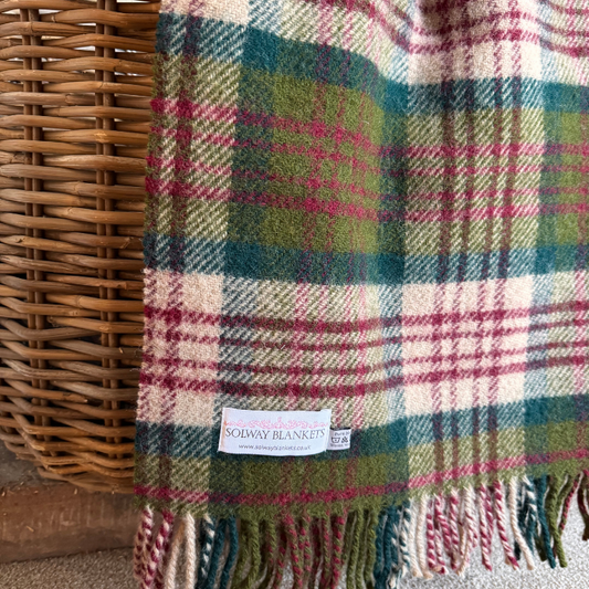 The Thistleberry Tartan check knee blanket hanging over a wicker basket