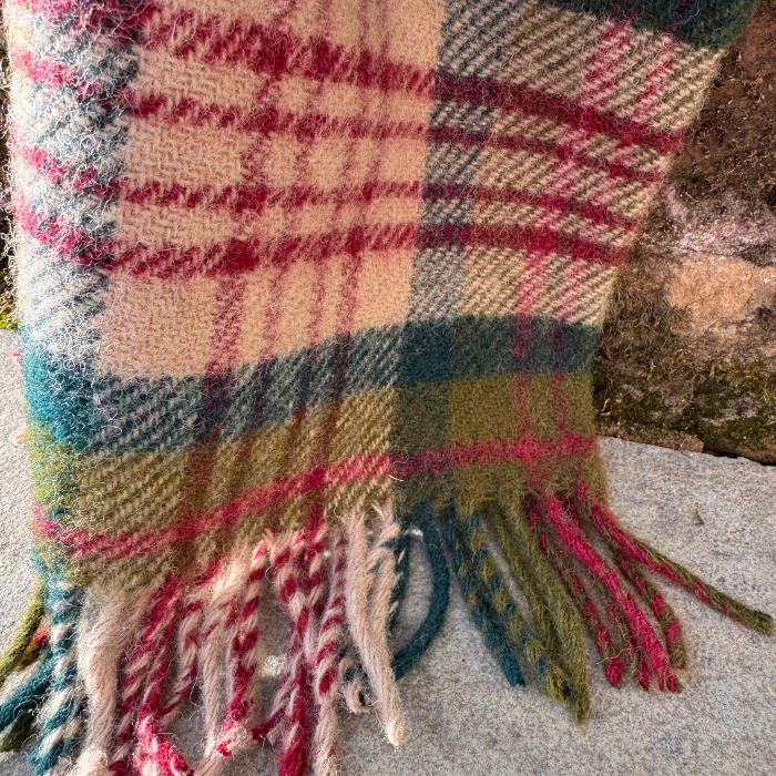 A close-up of a folded plaid fabric, featuring the Thistleberry check pattern with red, greens and teal against a oatmeal beige backgroud