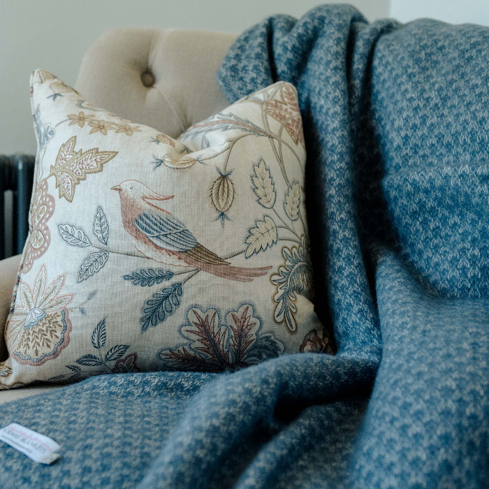 Decorative pillow with floral and bird pattern on a twilight blue textured woollen throw placed on a beige chair