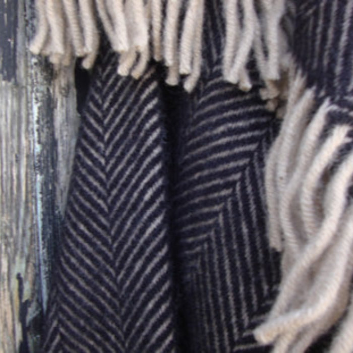 Charcoal and beige herringbone patterned blanket with fringes on a wooden surface