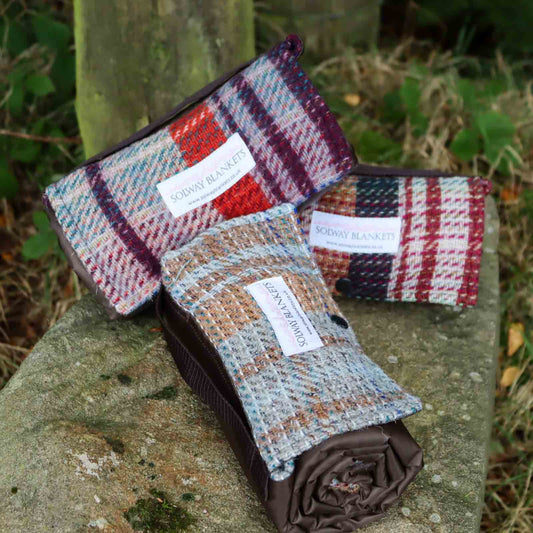 Three Random Recycled Waterproof Walker’s Companion Blanket rolled up on a stone
