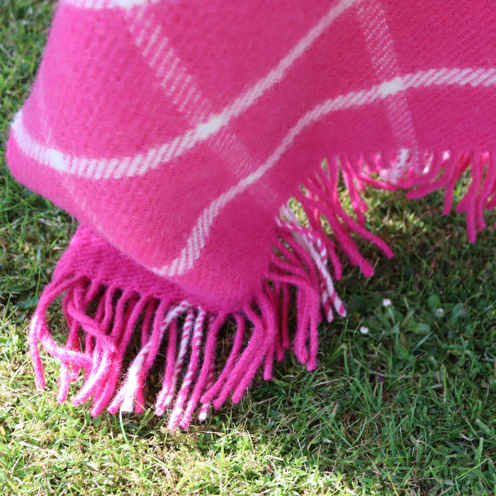 Close up of a pink plaid wool blanket with white stripes draped over grass