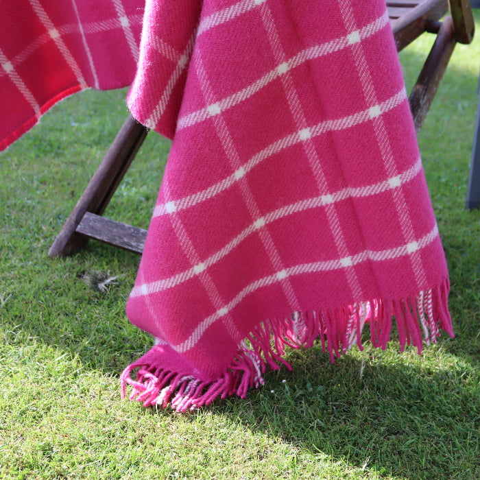 Pink plaid wool blanket with white stripes draped over a chair on a grassy outdoor setting
