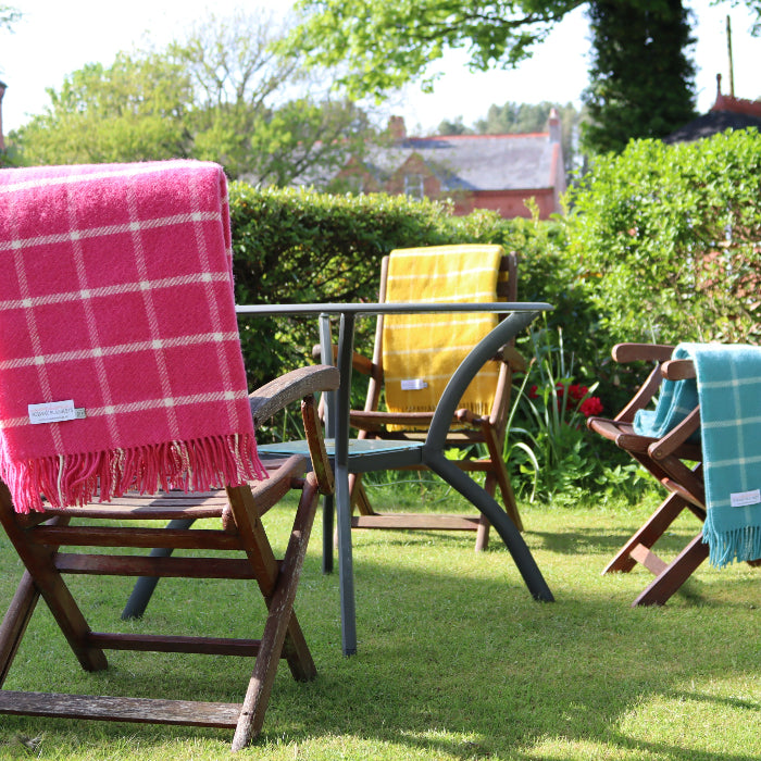 Pink and white checkered wool blanket draped over chair alongside two differently coloured blankets in a garden setting