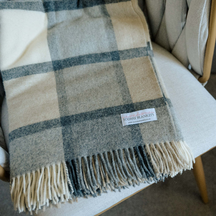Folded plaid throw with soft grey and white tones draped over a chair with a Solway Blankets label. 