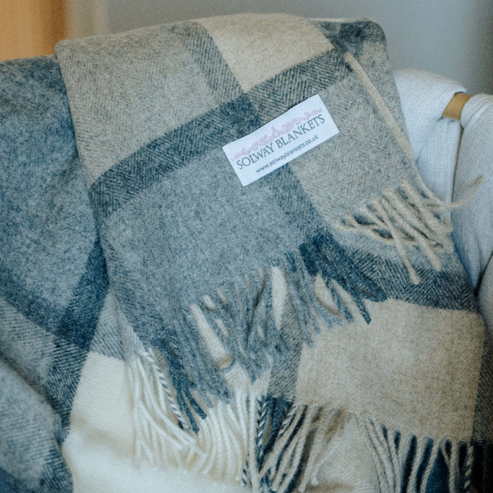 Folded soft grey and white plaid throw with fringes on a chair, featuring a Solway Blankets label.