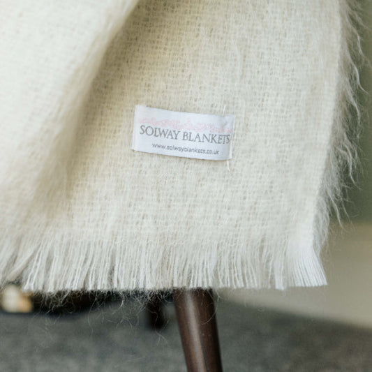 Close-up of a Winter White Mohair Throw with a Solway Blankets label on a blurred background