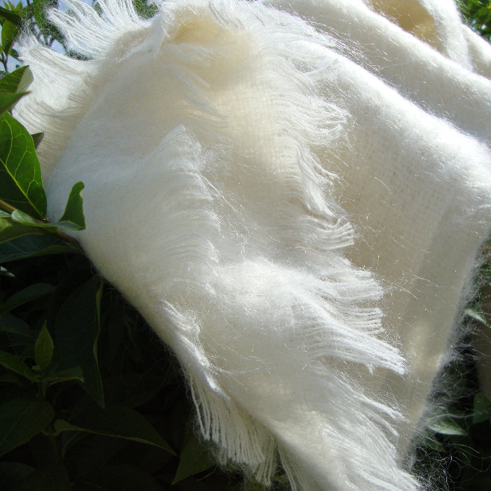 Close-up of Winter White Mohair Throw with fringes against a green leafy background