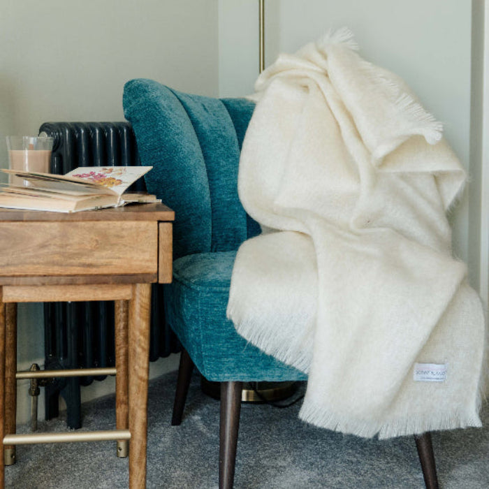 Blue chair with a plain Winter White Mohair Throw blanket draped over it in a room setting.