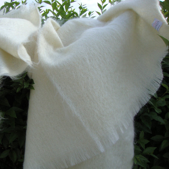 Winter White Mohair Throw Blanket with fringes draped over a surface with green leaves in the background