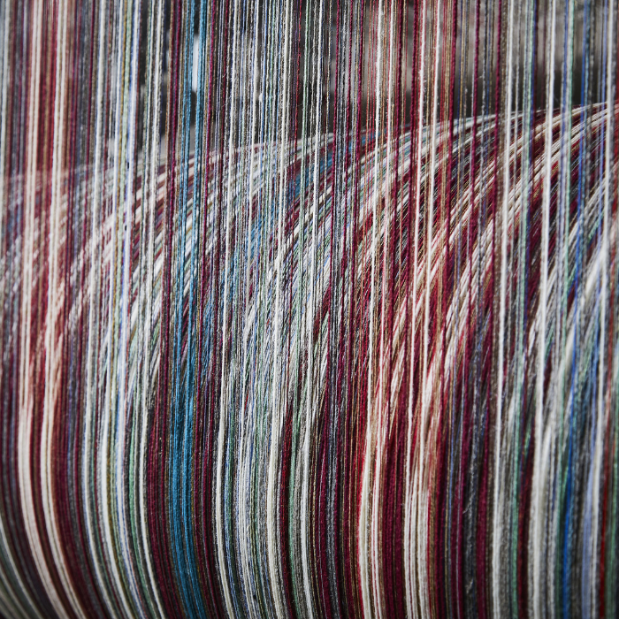 Close-up of multicoloured yarn strands separated over a drum reading for the warping process and setting of the loom for weaving blankets