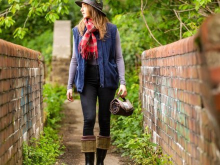 Lady with hat and scarf walking in countryside with picnic blanket roll