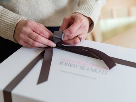 hands tying ribbon on gift boxed blanket