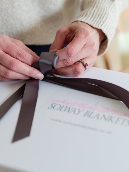 hands tying ribbon on gift boxed blanket