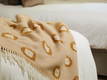 Lion merino wool baby blanket in tan colours, draped over bed