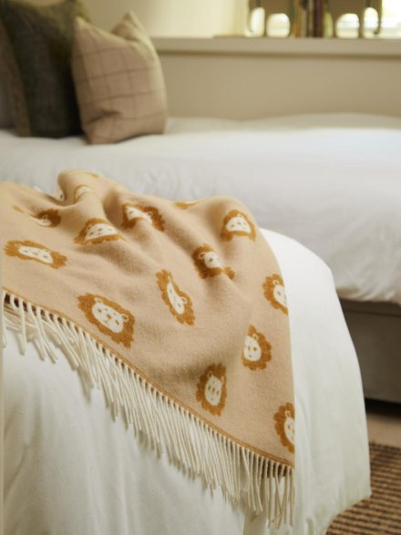 Lion merino wool baby blanket in tan colours, draped over bed